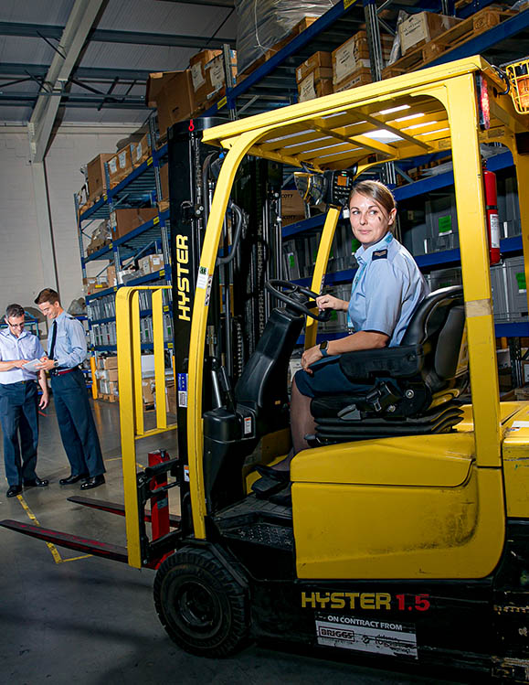 Female RAF Supplier operating forklift in storage warehouse with racking