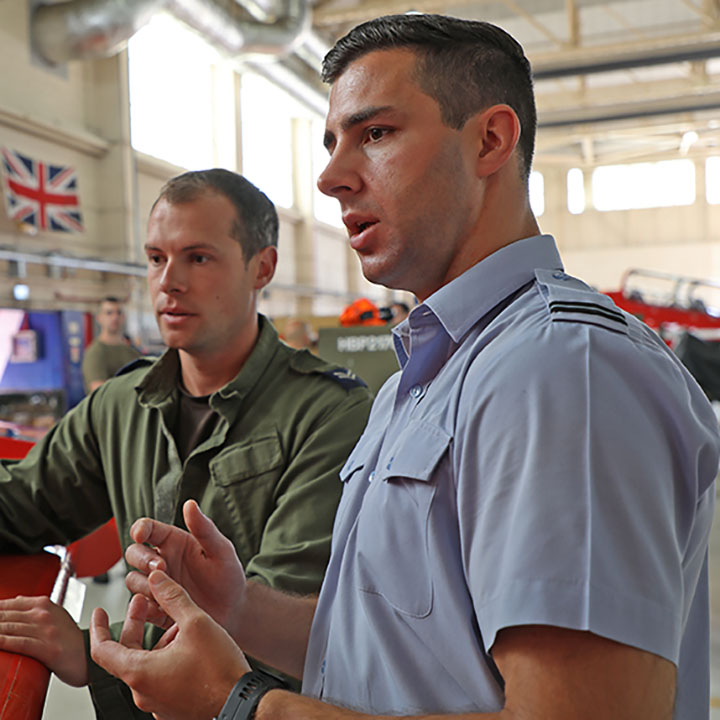 RAF Engineering Officer (Aero Systems) briefing RAF Aircraft Technician (Mechanical), stood by red Hawk jet in Red Arrows hangar