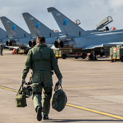 RAF Pilot carrying equipment walking out to line of FGR4 Typhoon jets on concrete apron