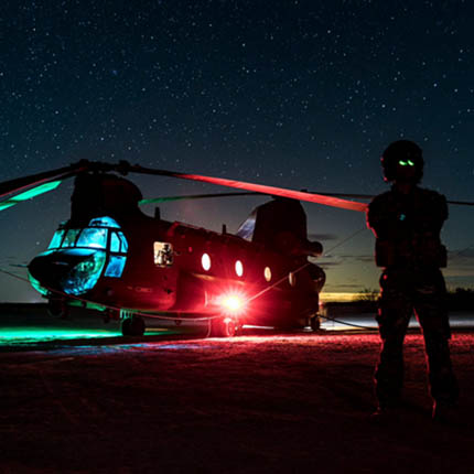 RAF Weapon Systems Operator Crewman in front of illuminated Chinook helicopter at night