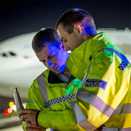 RAF Police in hi-vis inspecting tablet on aircraft apron at night