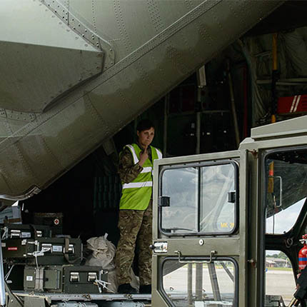 RAF Logistics Officer directing RAF mover using telehandler to load equipment onto cargo aircraft's rear ramp