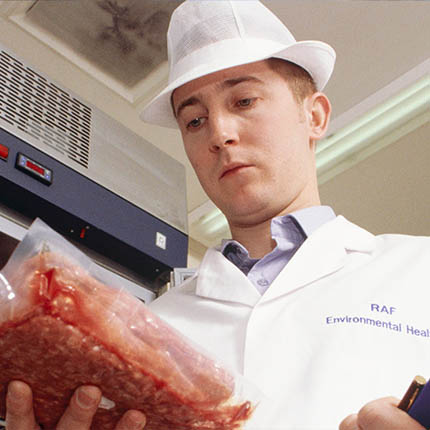 RAF Environmental Health Practitioner in protective clothing examining pack of meat