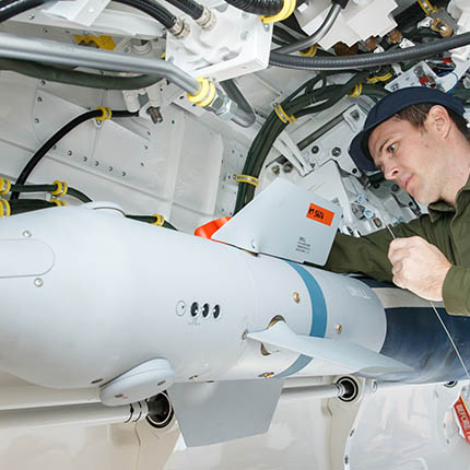 RAF Weapon Technician working on guided bomb underneath aircraft