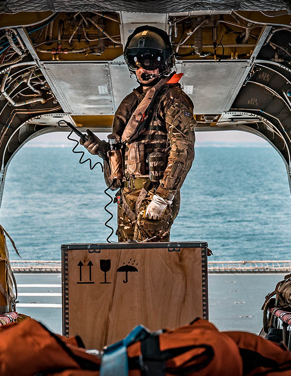 RAF Weapon Systems Operator (Crewman) securing cargo in rear of Chinook helicopter aboard Navy aircraft carrier
