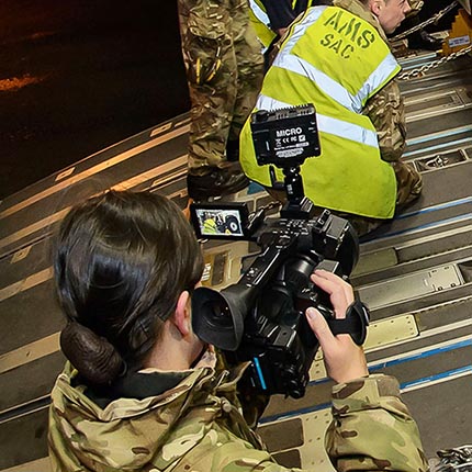 Media Operations specialist filming RAF movers securing load on aircraft ramp