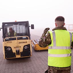 RAF mover marshalling colleague driving air cargo tow truck on apron