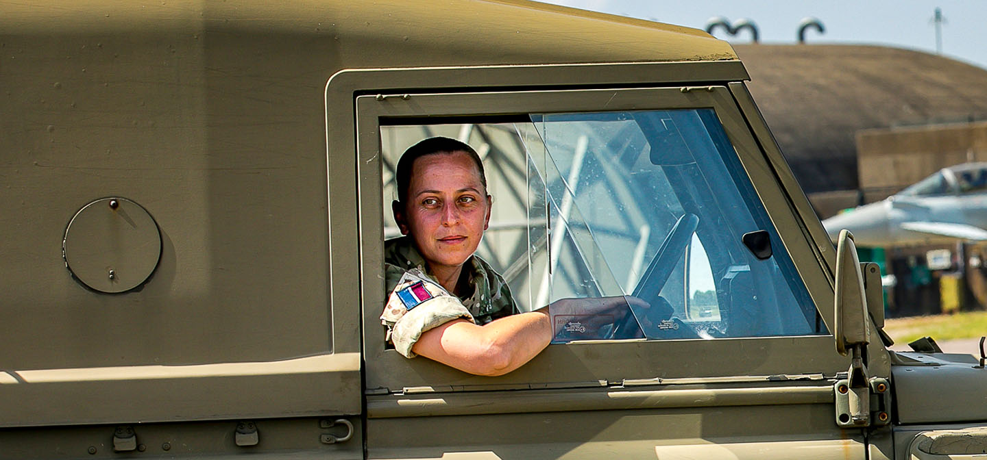 Female RAF Driver driving Land Rover along airfield taxi-way in front of Typhoon jet