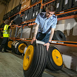 RAF Supplier rolling spare aircraft tyre along floor in warehouse