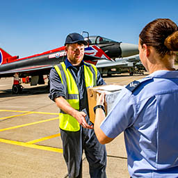 RAF Supplier Corporal handing package to RAF Aircraft Technician by RAF Display Team Typhoon jet in "Blackjack" livery