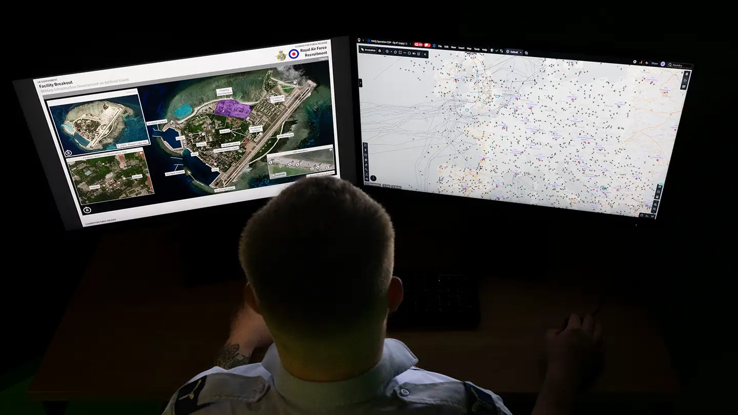 RAF Intelligence Analyst studying aerial photograph of airfield on computer monitors