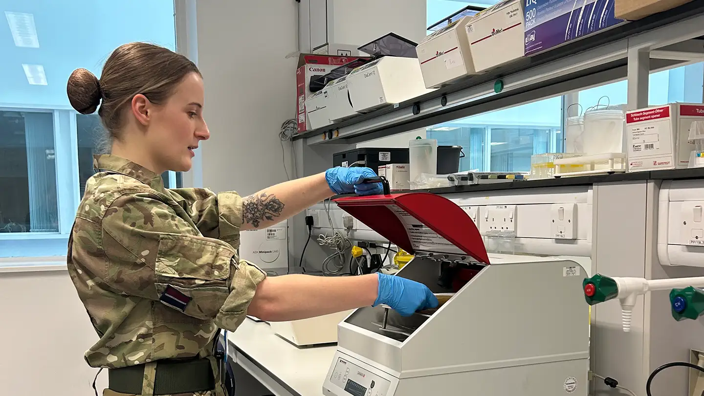 RAF Biomedical Scientist inserting sample tray into analysis machine in laboratory